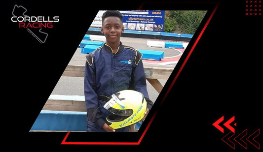 A young Cordell in a blue and yellow suit, holding a yellow "Buckmore Park" helmet, standing by a race track.